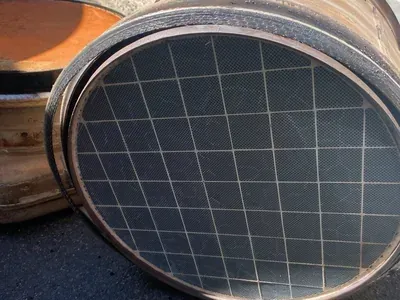 A close-up view of a circular automotive catalytic converter with a visible grey honeycomb ceramic core and metal casing.