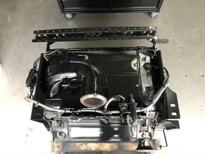 A black, industrial automotive seat assembly unit viewed from above, featuring metal tracks and electrical wiring.