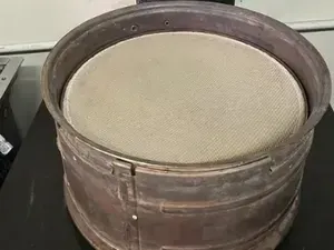 A laboratory sieve shaker machine with a round metal sieve mounted on its platform under a control panel with two gauges.