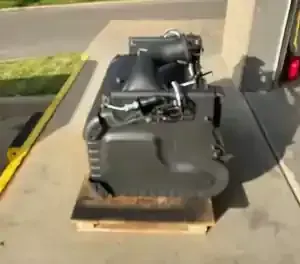 A dark gray, box-shaped industrial machine component sits on a wooden pallet outside a building.
