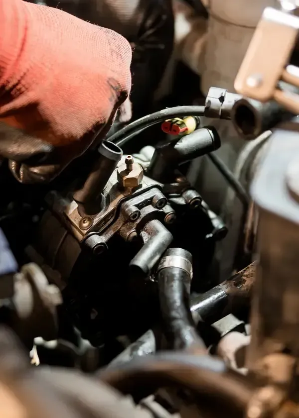 Close-up of hands wearing red gloves working on a car engine, connecting black hoses to a metallic fuel component.
