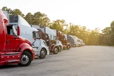 Rows of white semi-trucks parked in two lines facing each other under a blue sky with white clouds.