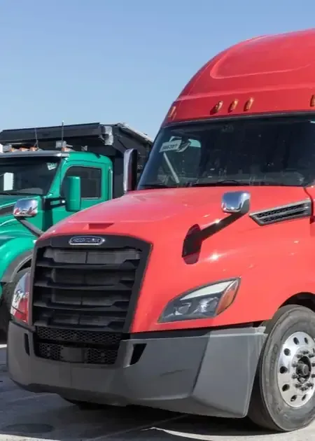 A bright red semi-truck parked next to a green dump truck under a clear blue sky.