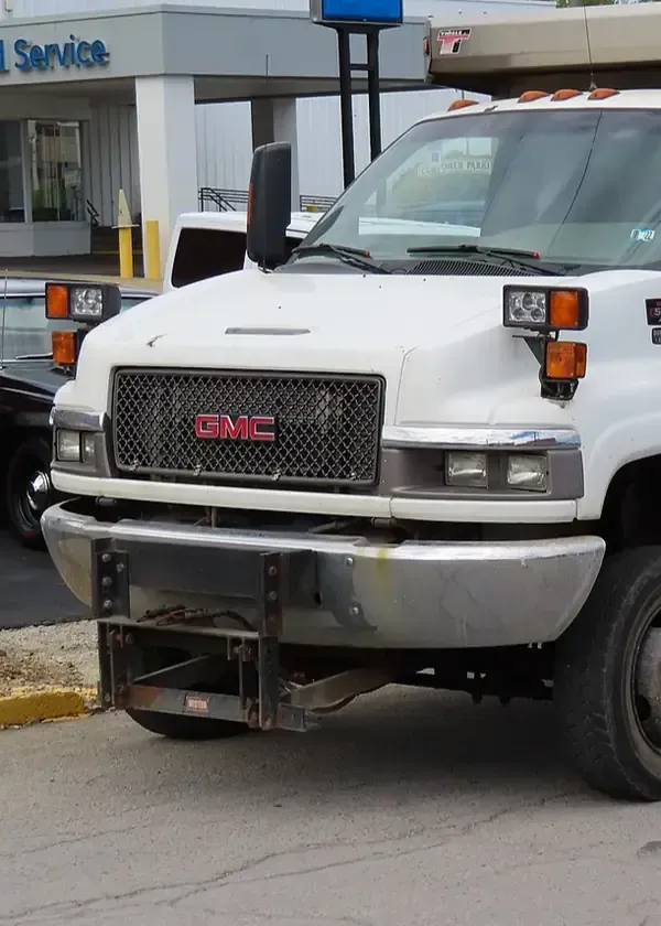 White GMC commercial truck parked outside, featuring a front-mounted snow plow attachment.