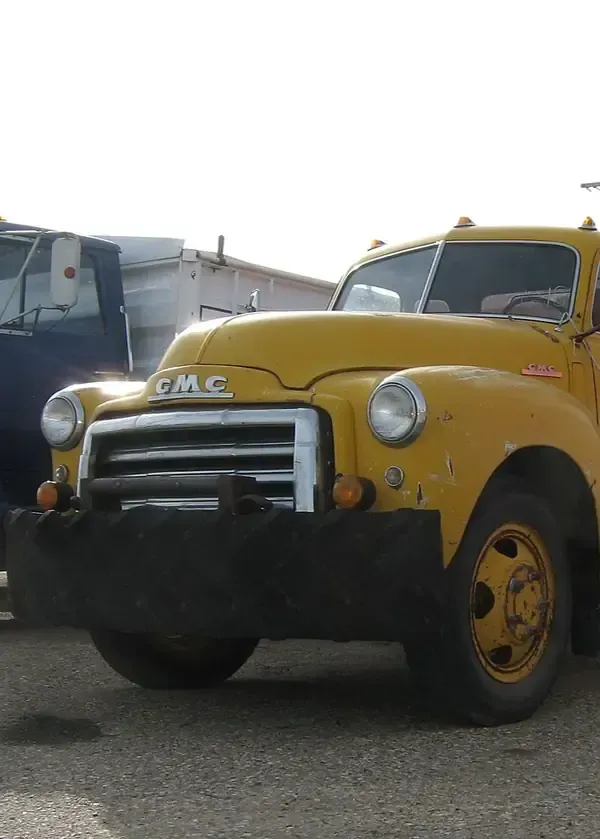 A yellow vintage GMC truck with a heavy-duty black bumper parked outdoors.