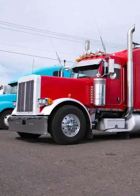 A red semi-truck parked outdoors, with a blue truck partially visible behind it.
