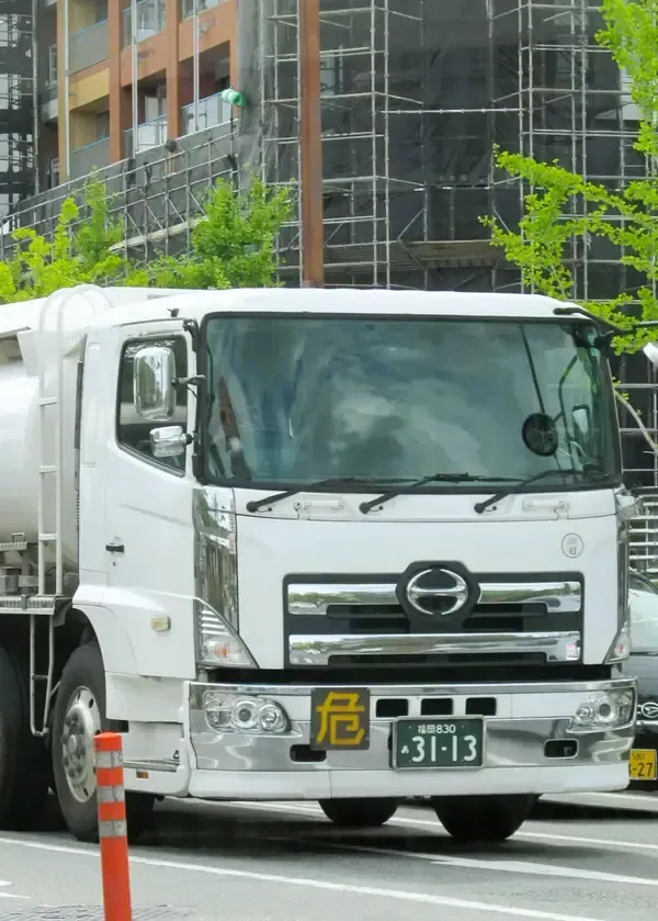 A white Hino fuel tanker truck stopped on a city street, displaying a yellow 