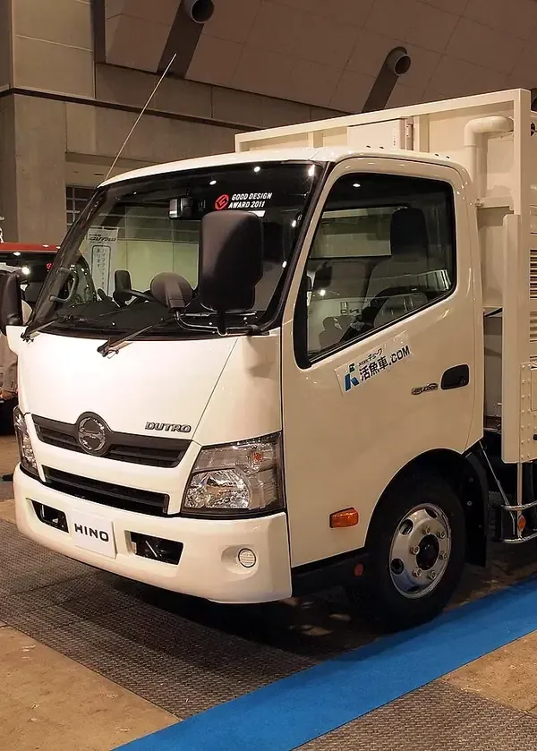 A white Hino light-duty commercial truck parked indoors on a blue floor mat.