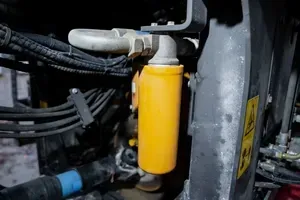 A yellow cylindrical hydraulic filter mounted on the side of a piece of heavy industrial machinery.