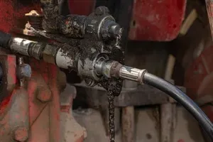 A dirty, oil-covered hydraulic hose connection on a piece of truck.