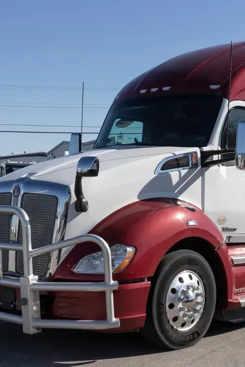 A white and maroon semi-truck with a silver metal bumper guard parked under a clear blue sky.