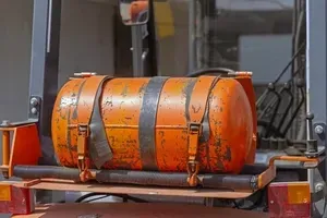 A cylindrical orange propane tank mounted securely to the back of a tractor.