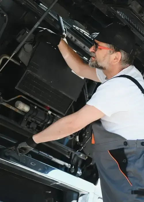 A person in a high-visibility jacket and white hard hat points at a computer monitor in an industrial control room.
