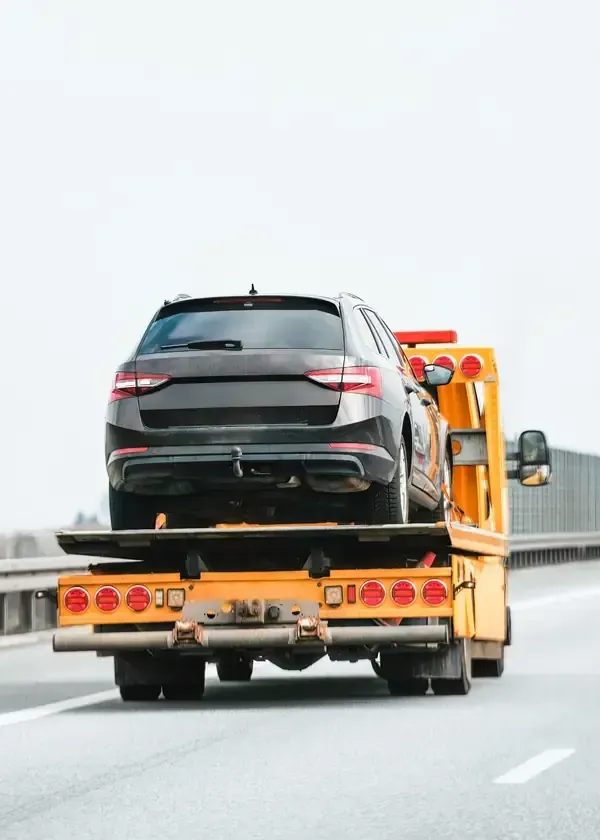 A dark gray SUV being transported on the back of a yellow tow truck traveling along a highway.