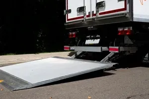 A white box truck with its rear liftgate lowered to the pavement for loading or unloading.