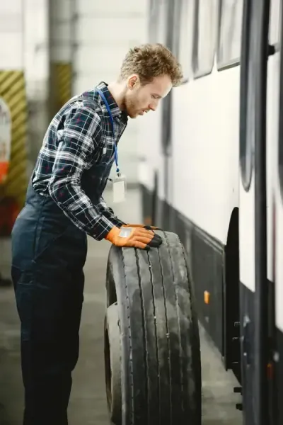A person wearing work clothes and gloves inspects a large vehicle tire in a maintenance garage.