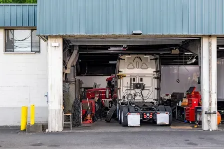 A semi-truck parked in an open service garage bay with tools and equipment nearby.