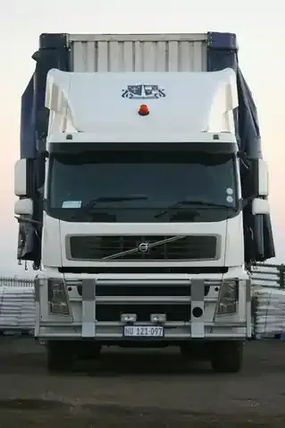 A white Volvo semi-truck parked outdoors, viewed from the front, with blue curtains and a roof deflector.