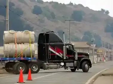 A black semi-truck with red racing stripes transports two large, stacked plastic tanks on a flatbed trailer.