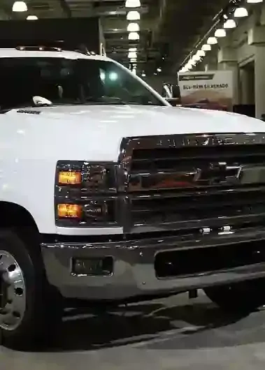 Close-up of a white Chevrolet Silverado truck parked inside a bright, industrial showroom.