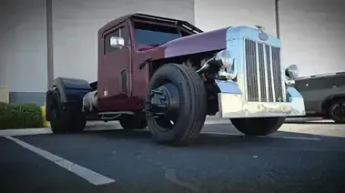 A custom maroon Peterbilt semi-truck with a chopped roof parked in an outdoor lot.