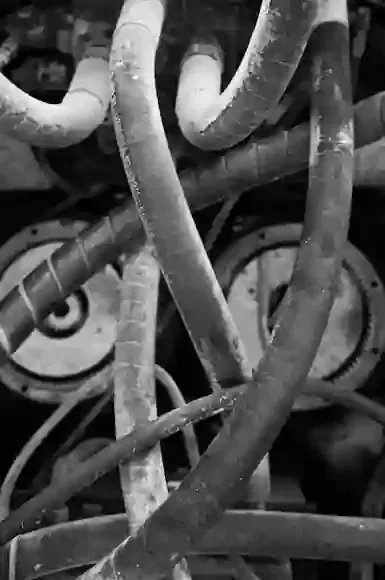 A black-and-white close-up of tangled industrial hydraulic hoses and mechanical machinery parts.
