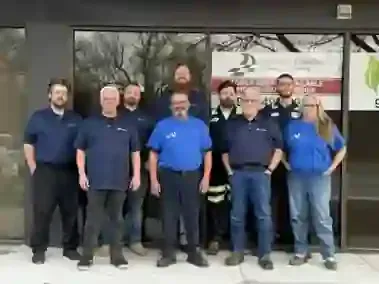 A group of employees in blue company shirts pose together in front of a Champion Fleet Care business window.