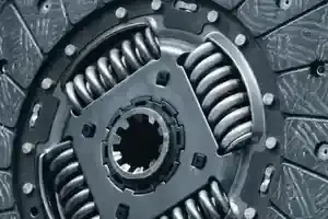 A close-up of a metal car clutch disc, showing its splined center hub, internal torsion springs, and friction material.