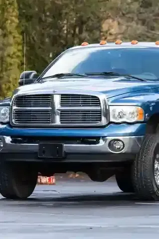A blue Dodge Ram pickup truck parked on pavement with trees in the background.