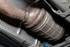 A metallic DPF is connected to an exhaust pipe, positioned above a textured silver heat shield.