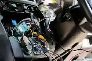 The dashboard of a vehicle with its center console panel removed, revealing a tangled mess of colorful electrical wiring.