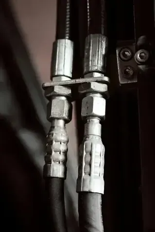 Two black hydraulic hoses with silver metal crimped fittings connected to a bracket.