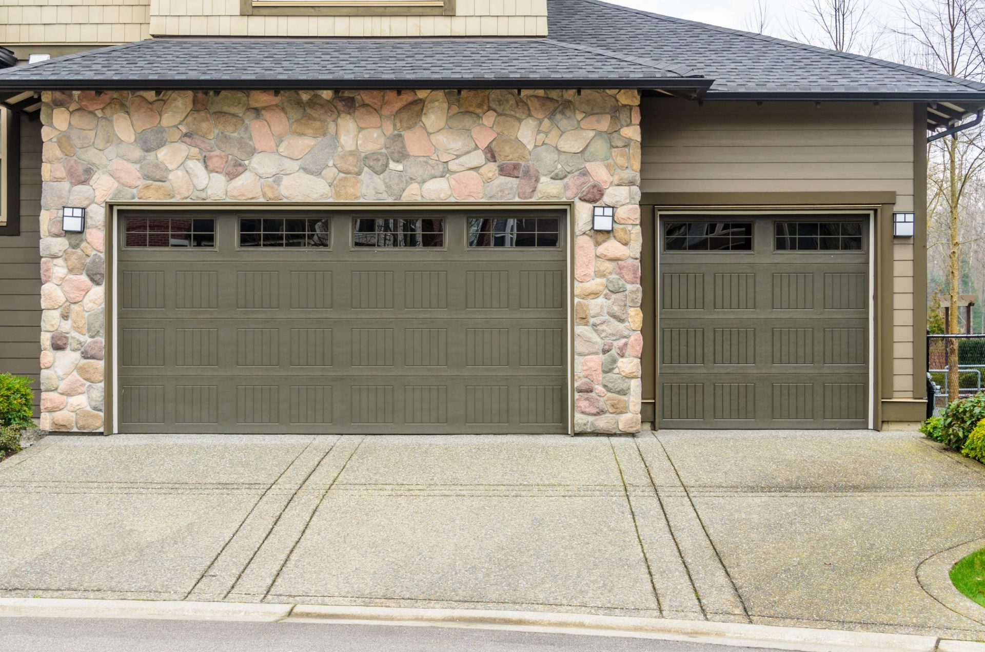 Garage with stone facade and olive green doors. Concrete driveway.