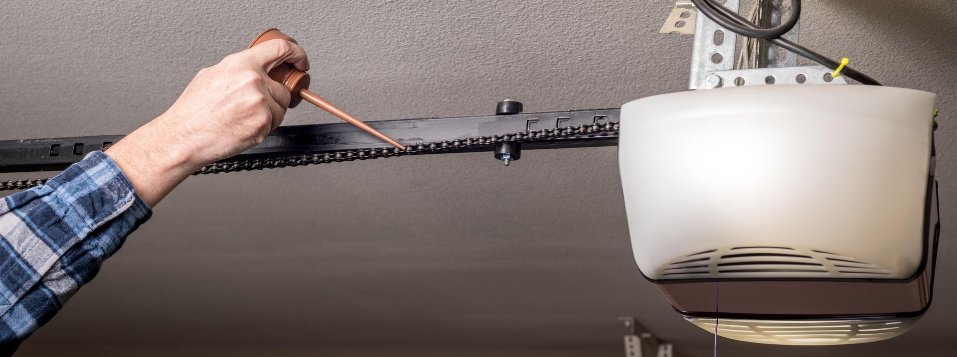 A person with a screwdriver is working on a garage door opener.
