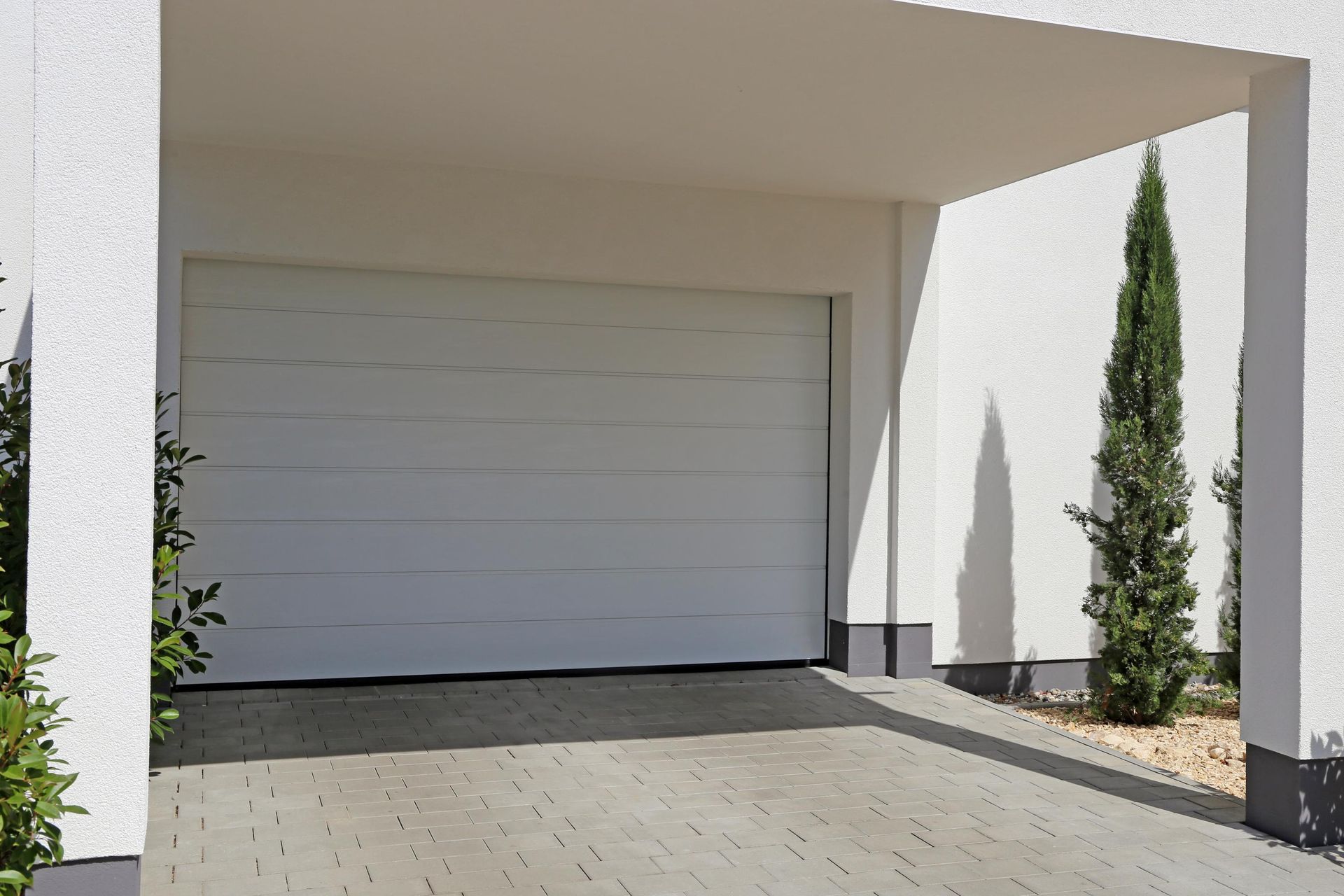 White garage door under a white overhang; a tall, thin tree stands beside the entrance.