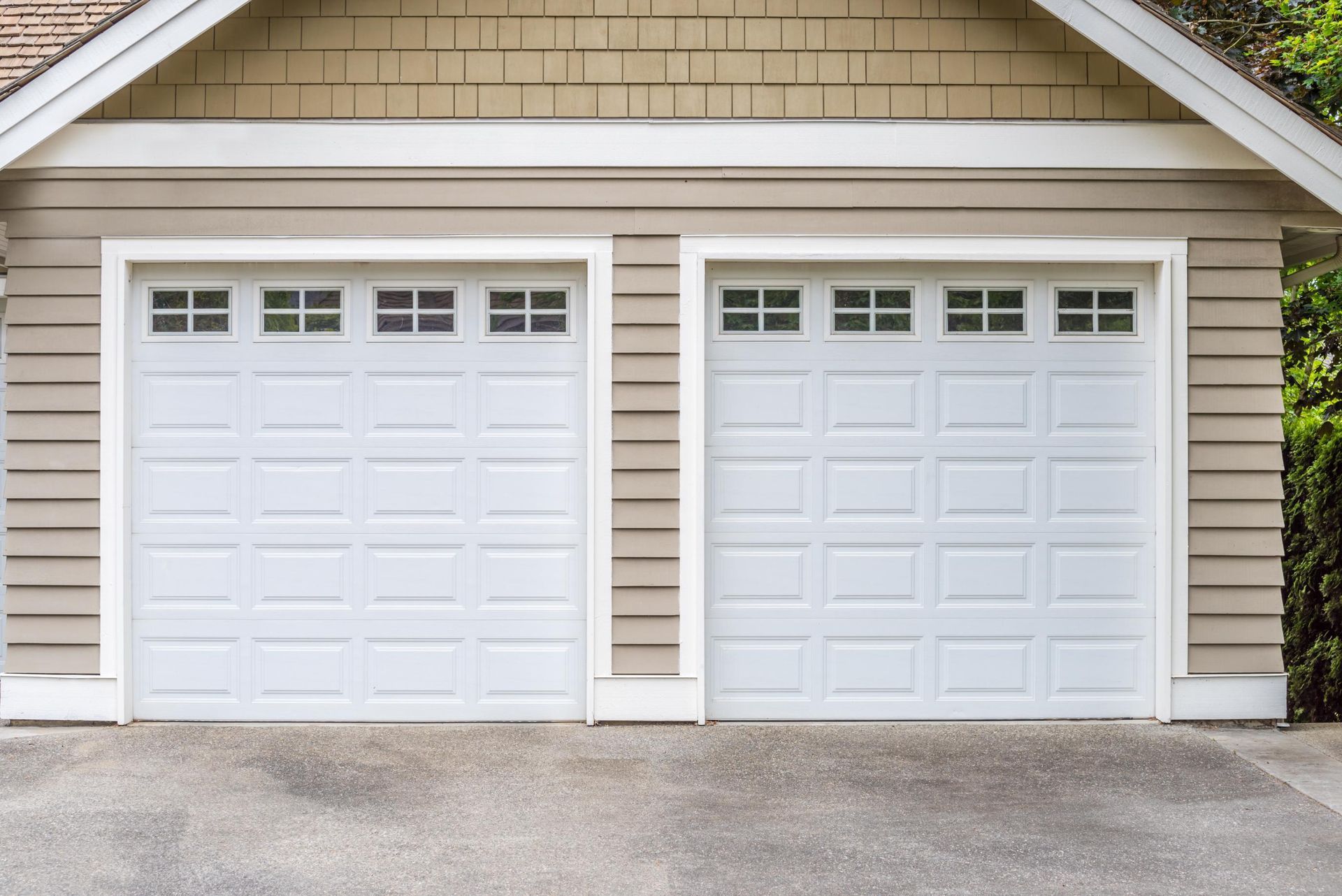 Two white garage doors with small windows, beige siding, and a concrete driveway.