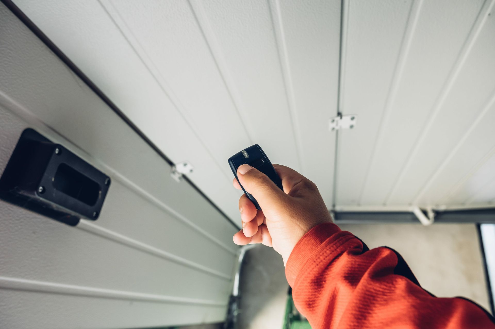 Hand using a remote control to operate a garage door opener.