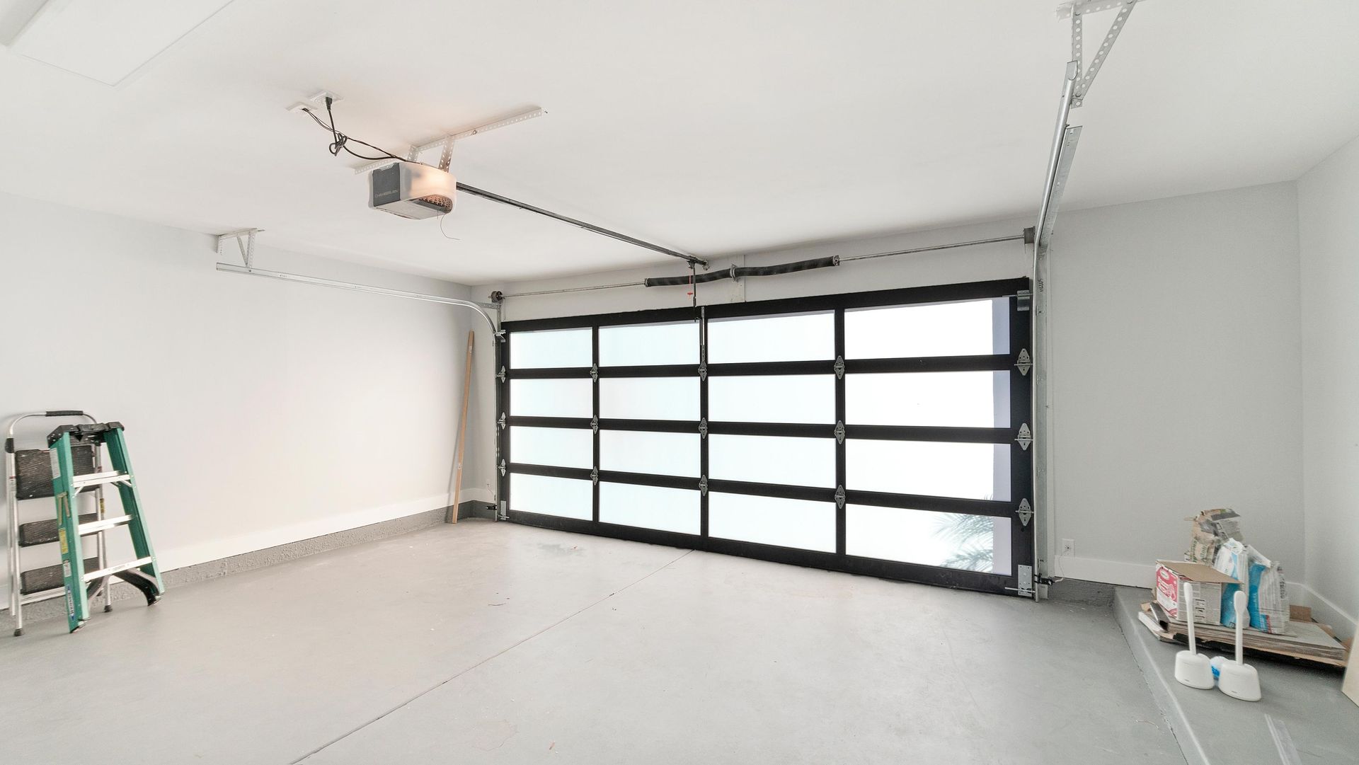 Modern, empty garage with glass garage door, white walls, and ladder.