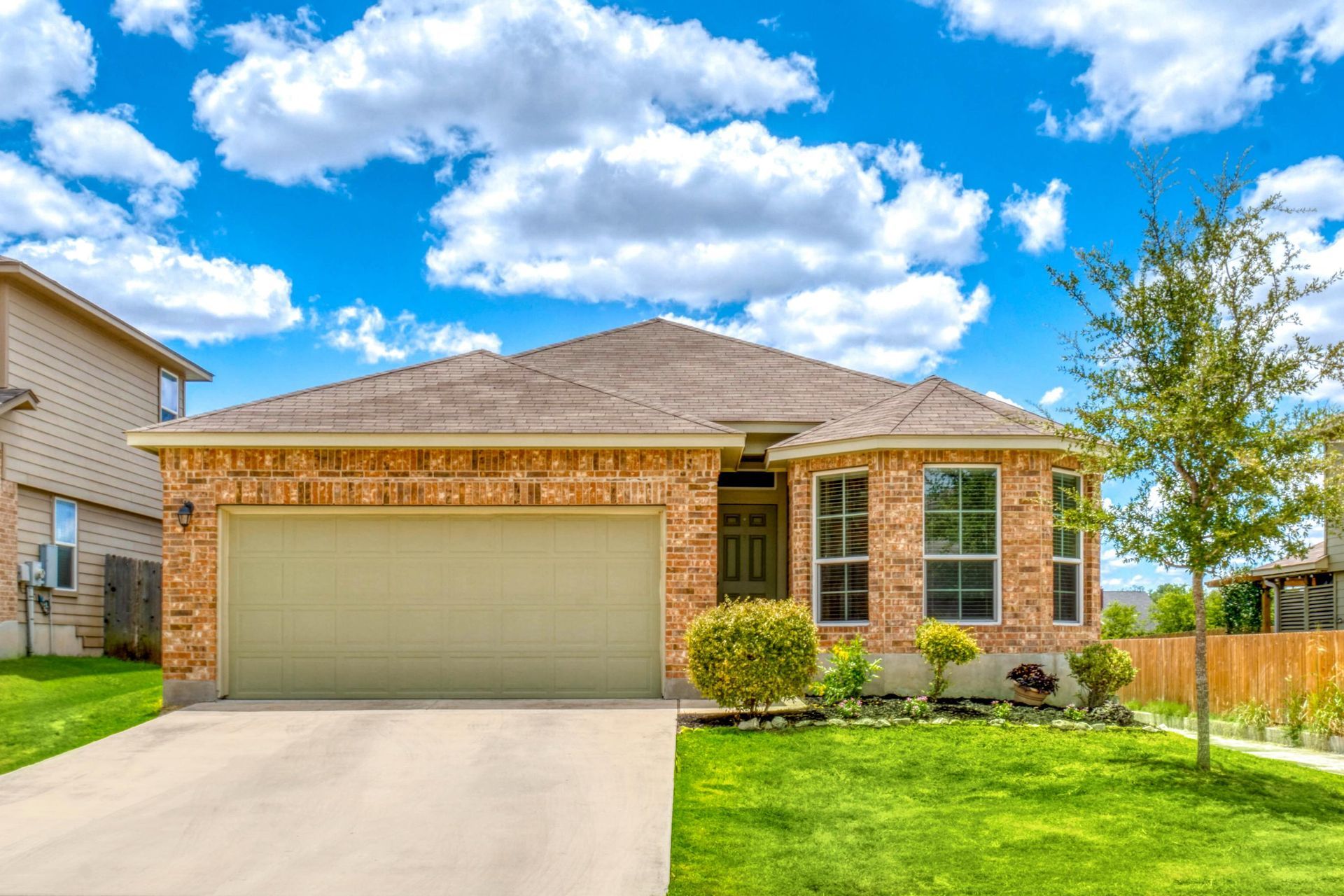 Brick house with a beige garage door, green lawn, and blue sky with fluffy clouds.