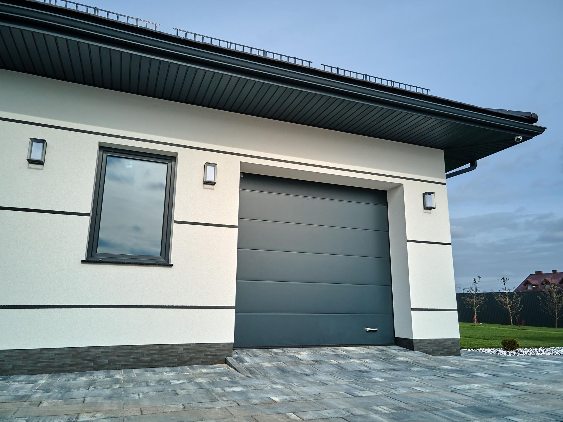 White and gray garage with gray door and window, surrounded by a paved driveway and grass.