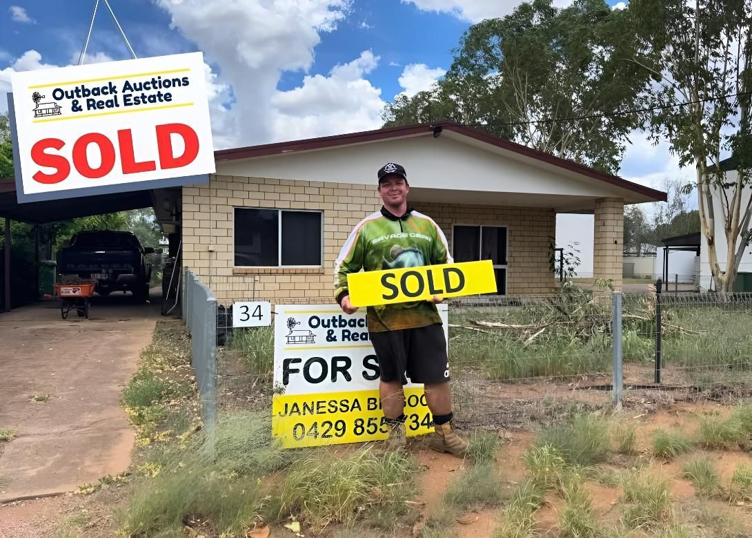A Man Is Holding A Sold Sign In Front Of A House — Outback Auctions and Real Estate in Cloncurry, QLD