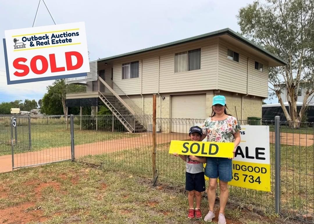 A Woman And A Child Are Holding A Sold Sign In Front Of A House — Outback Auctions and Real Estate in Cloncurry, QLD
