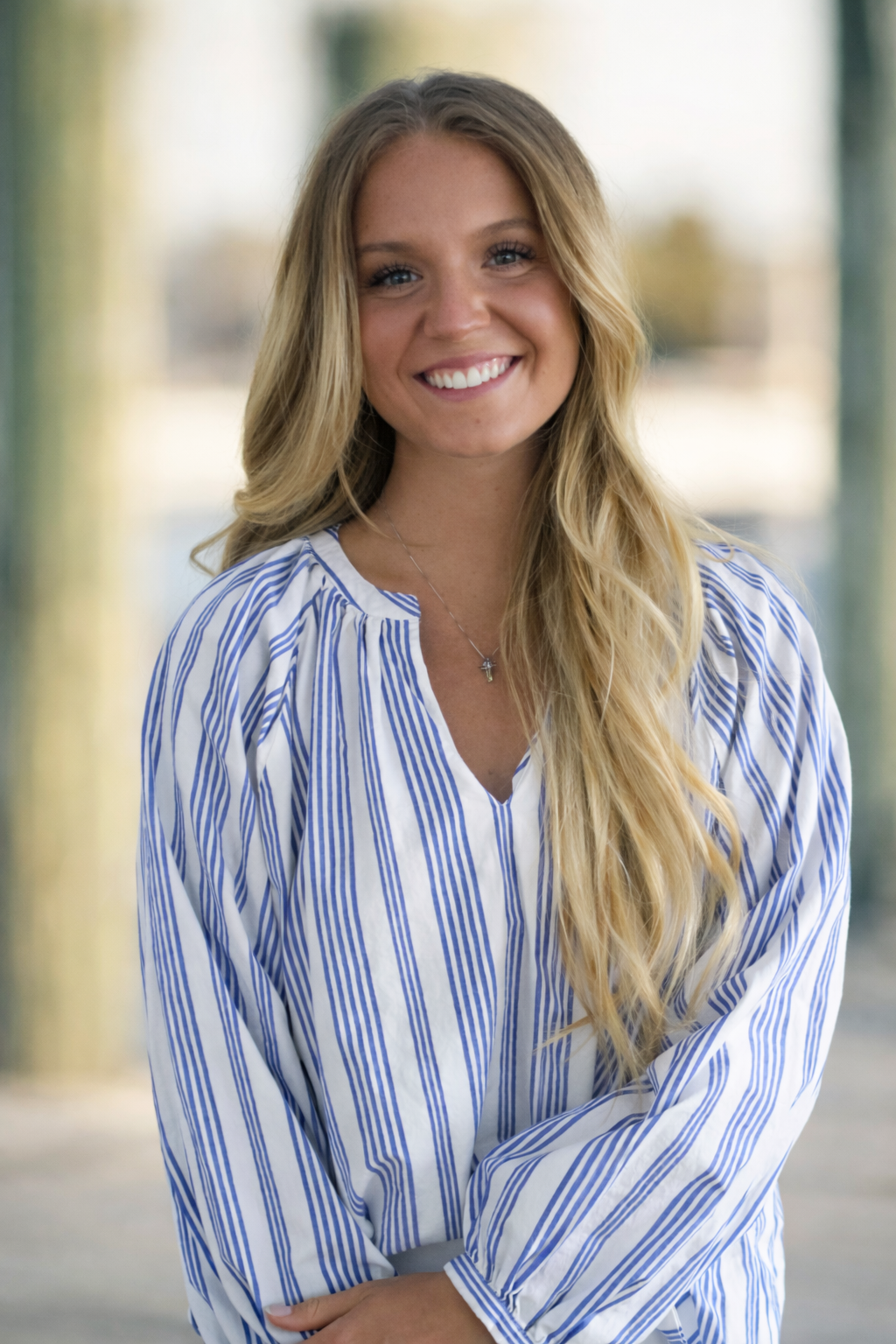 A woman wearing a blue shirt and a gold necklace is smiling for the camera.