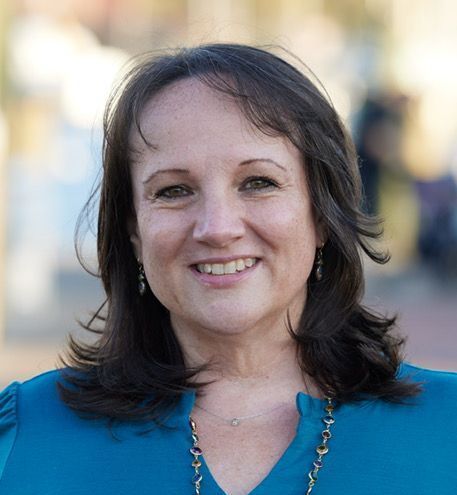 A woman wearing a blue shirt and a gold necklace is smiling for the camera.