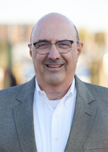 A bald man wearing glasses and a suit is smiling for the camera.