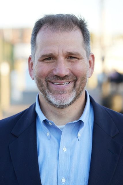 A man in a suit and blue shirt is smiling for the camera.