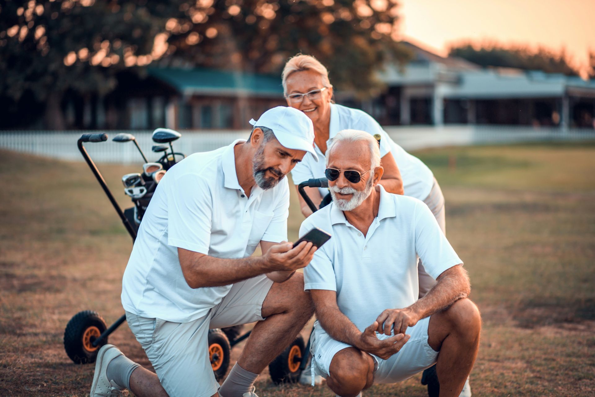 A group of older people are looking at a cell phone on a golf course.