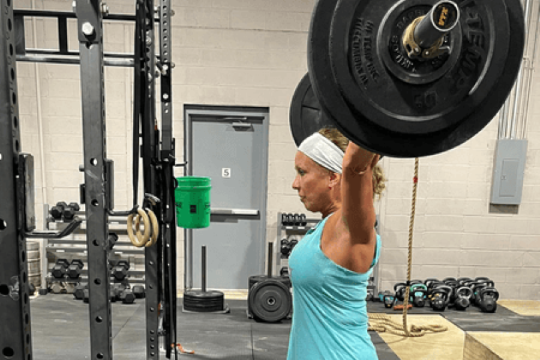 A woman is lifting a barbell over her head in a gym.