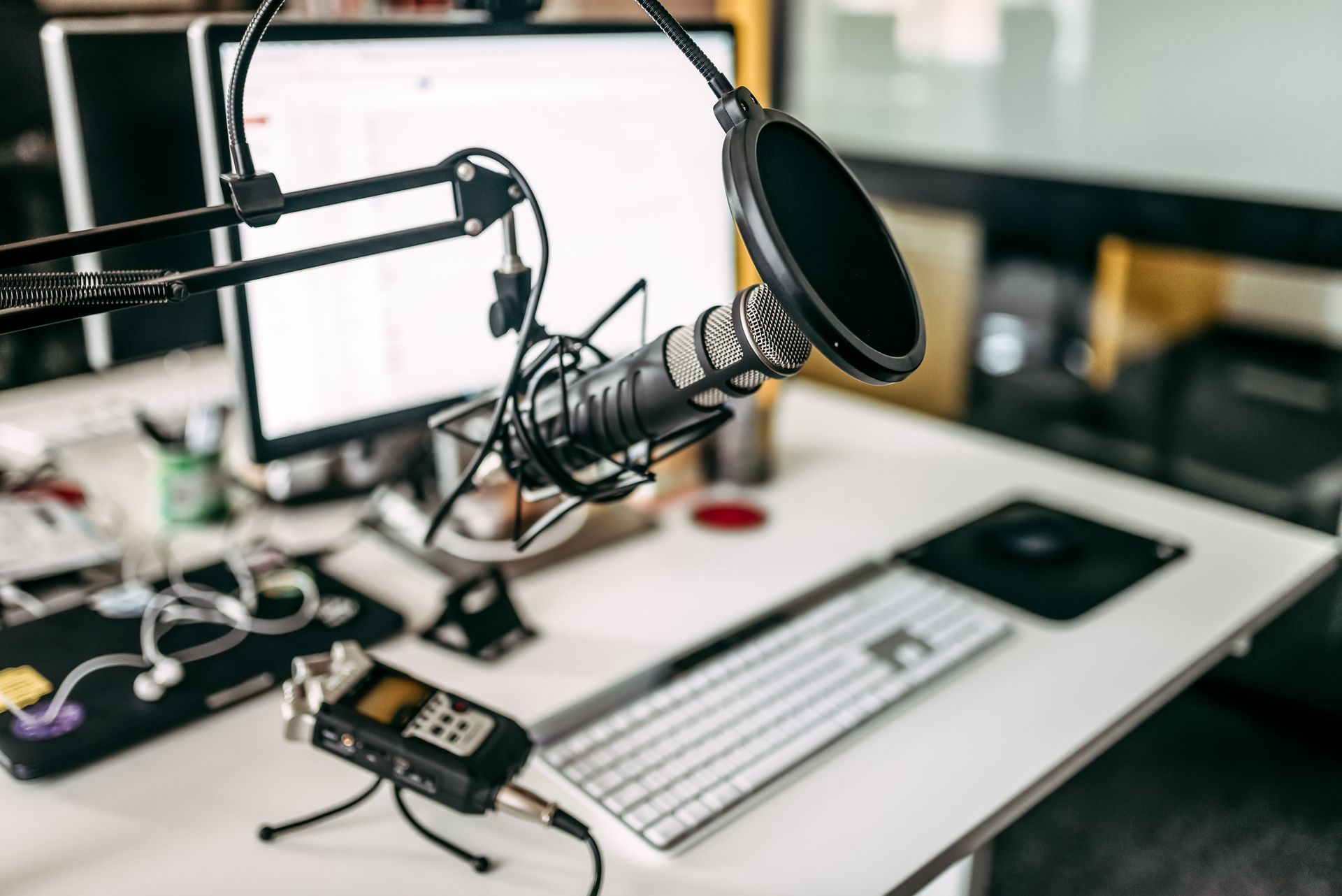Microphone setup on desk with computer, keyboard, and audio recorder; a home recording studio.