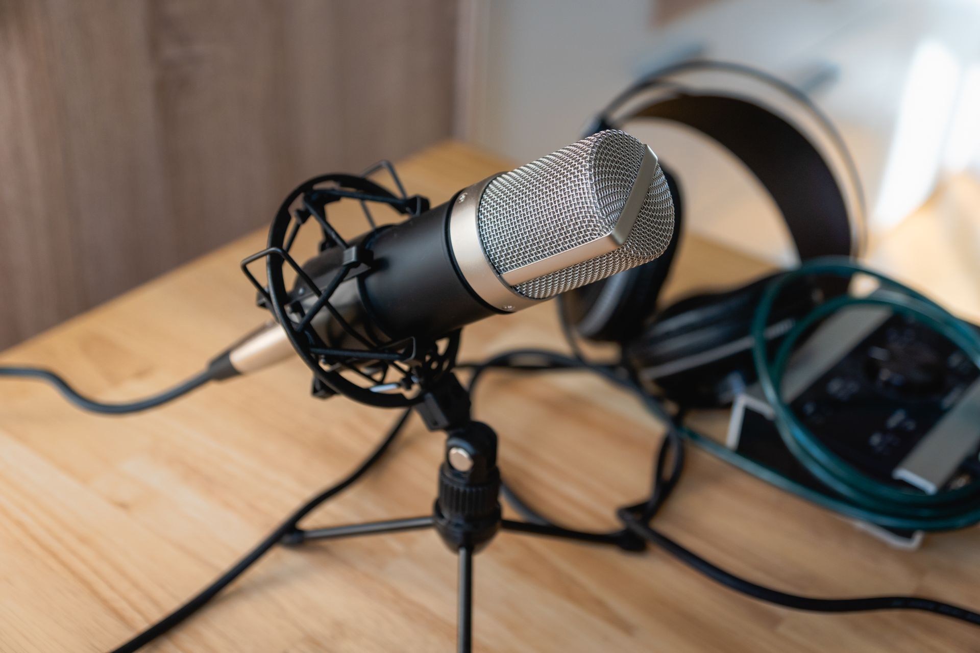 Microphone in a holder on a wooden table, with headphones and cables in the background.